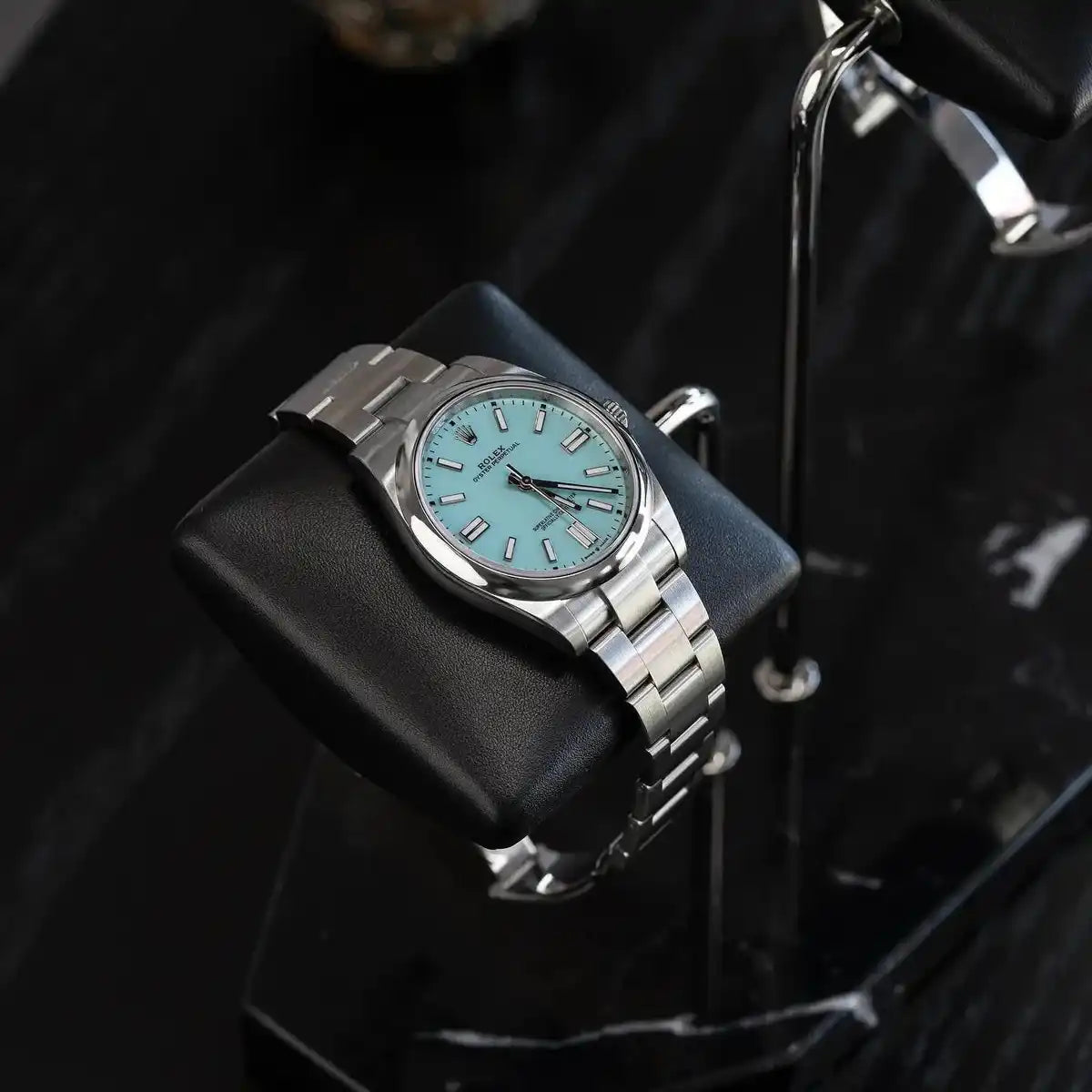 Silver Rolex Oyster Perpetual watch with turquoise dial.