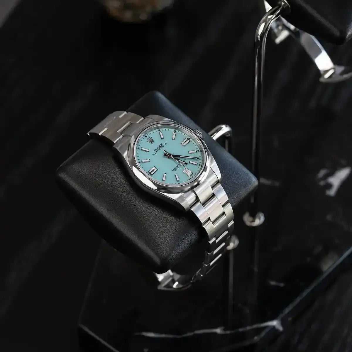 Silver Rolex Oyster Perpetual watch with turquoise dial.
