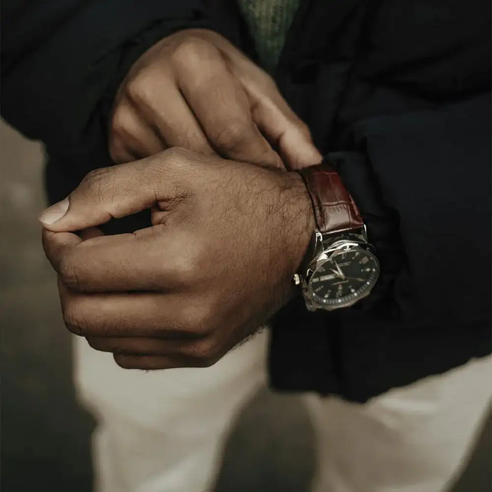 A classic analog wristwatch with a dark dial, silver-toned case and hands, paired with a rich brown leather strap.