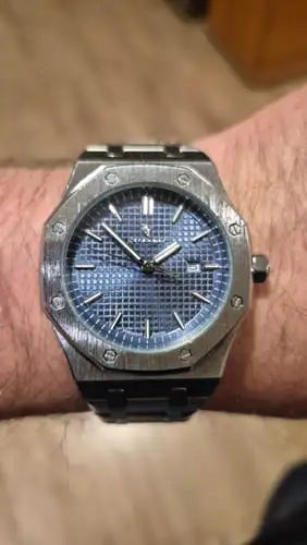 A silver-toned audemars piguet royal oak watch with a blue textured dial and black ceramic bracelet.