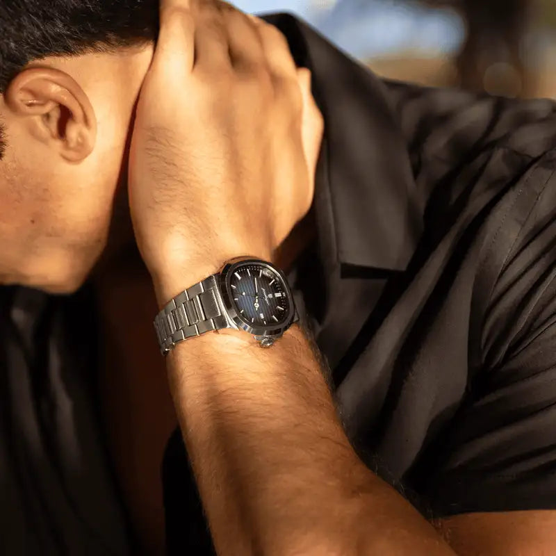 A sleek, silver-toned stainless steel watch with a dark gray dial and minimalist design worn on a man’s wrist.