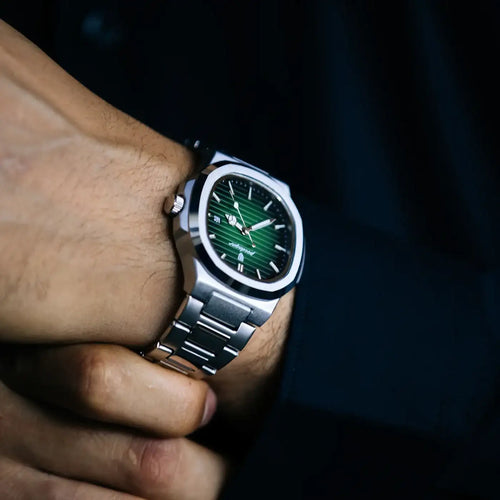 A sleek silver-toned stainless steel watch with a vibrant green gradient dial and minimalist white hour markers, worn on a person’s wrist.