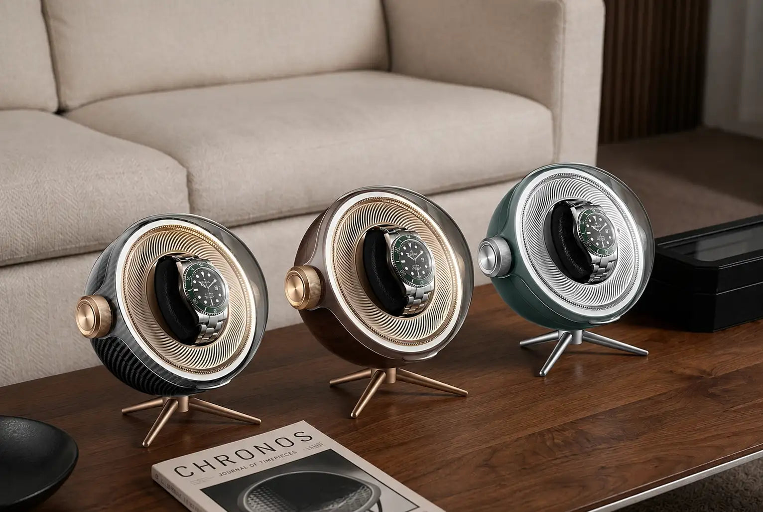 Three sleek, circular watch winder stands in metallic finishes, silver, bronze, and teal, with gold-tone accents and a ribbed design.